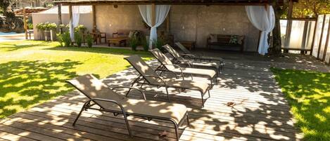 A wooden deck with lounge chairs and a covered seating area with a tiled roof.