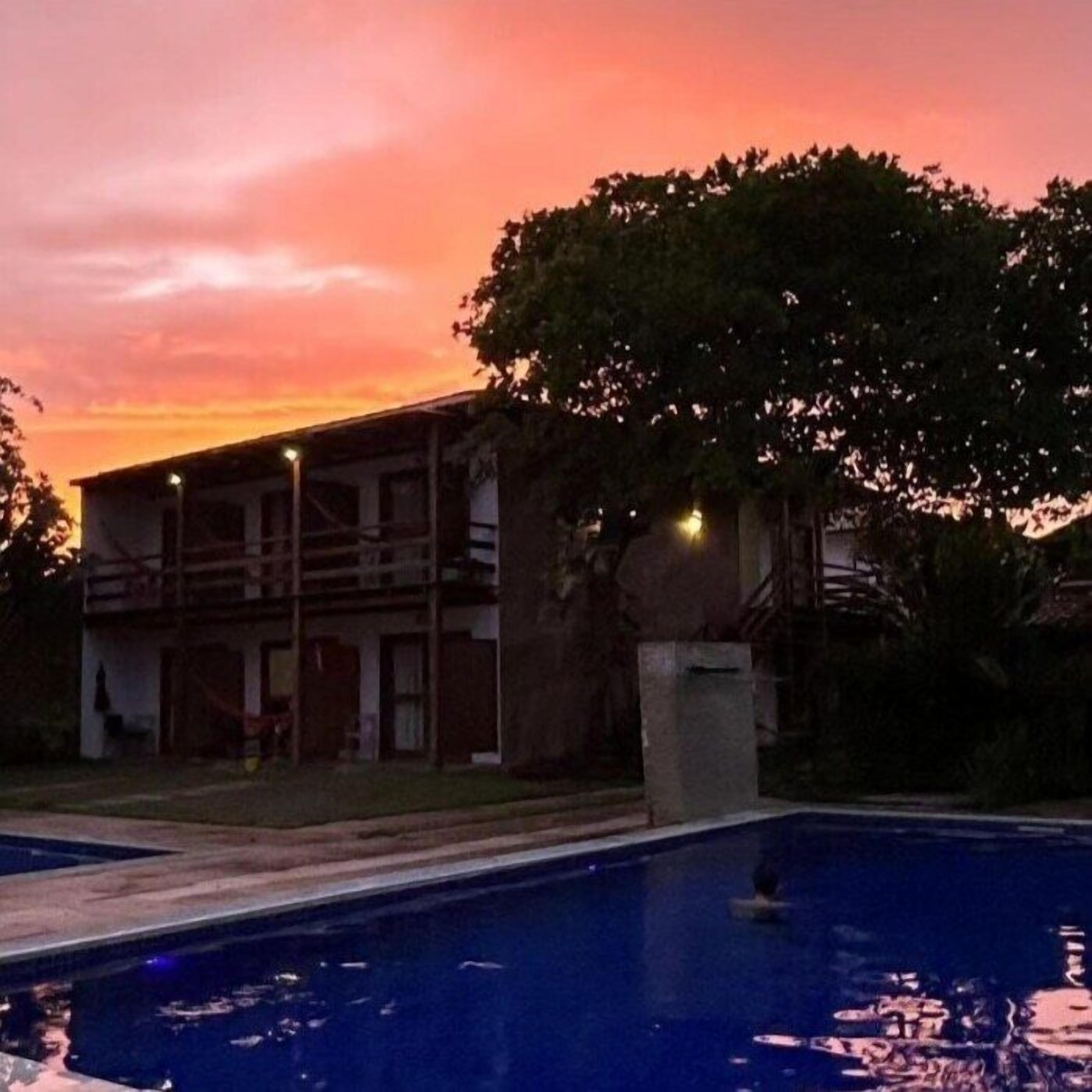 A building with a swimming pool, surrounded by trees and a sunset sky.