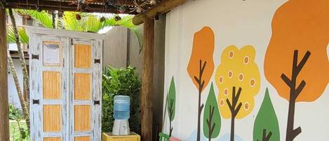 An outdoor patio area with a long white table, colorful chairs, and a mural of trees on the wall.