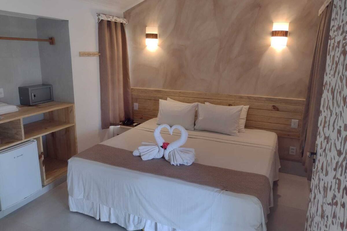 A hotel room with a wooden headboard, two bedside lamps, a bed with a white bedspread and pillows, a bedside table with a telephone, and a small desk with a microwave.