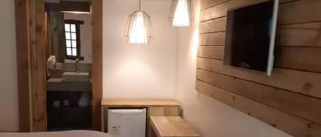 Un dormitorio compacto con cama, un escritorio pequeño, un televisor montado en una pared de madera e iluminación colgante.