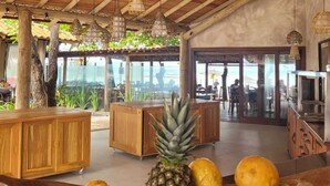 Un vaste espace intérieur doté d’un haut plafond en bois et de luminaires suspendus. On y trouve un comptoir en bois, avec un saladier rempli de fruits en premier plan.