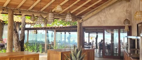 Amplio espacio interior con techo de madera alto y lámparas colgantes. En primer plano, una encimera de madera con un cuenco de frutas.