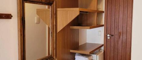 A room with a wooden shelving unit, a door, and a mirror on the wall.