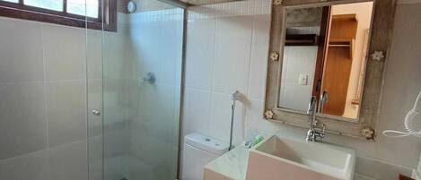 A bathroom with a glass shower enclosure, a toilet, a sink with a mirror, and a wooden ceiling.