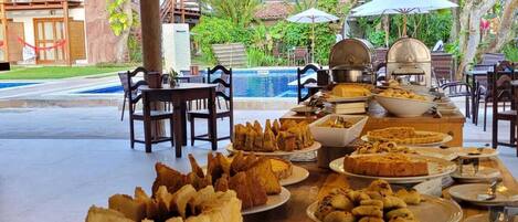 An outdoor buffet with various dishes and a pool in the background.