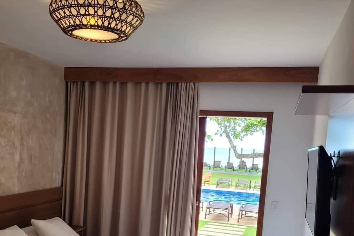 A hotel room with a large bed, a television, and a view of a pool and outdoor seating area.