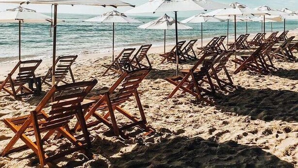 Une plage bordée de rangées de chaises longues en bois et de parasols blancs, donnant sur l’océan.