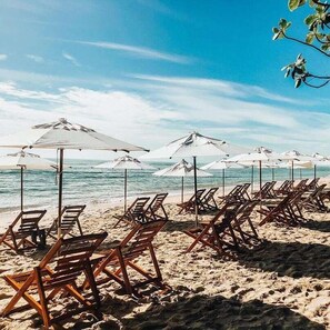 A beach with rows of wooden lounge chairs and white umbrellas, facing the ocean. - Aquarela Praia Hotel (Porto Seguro)