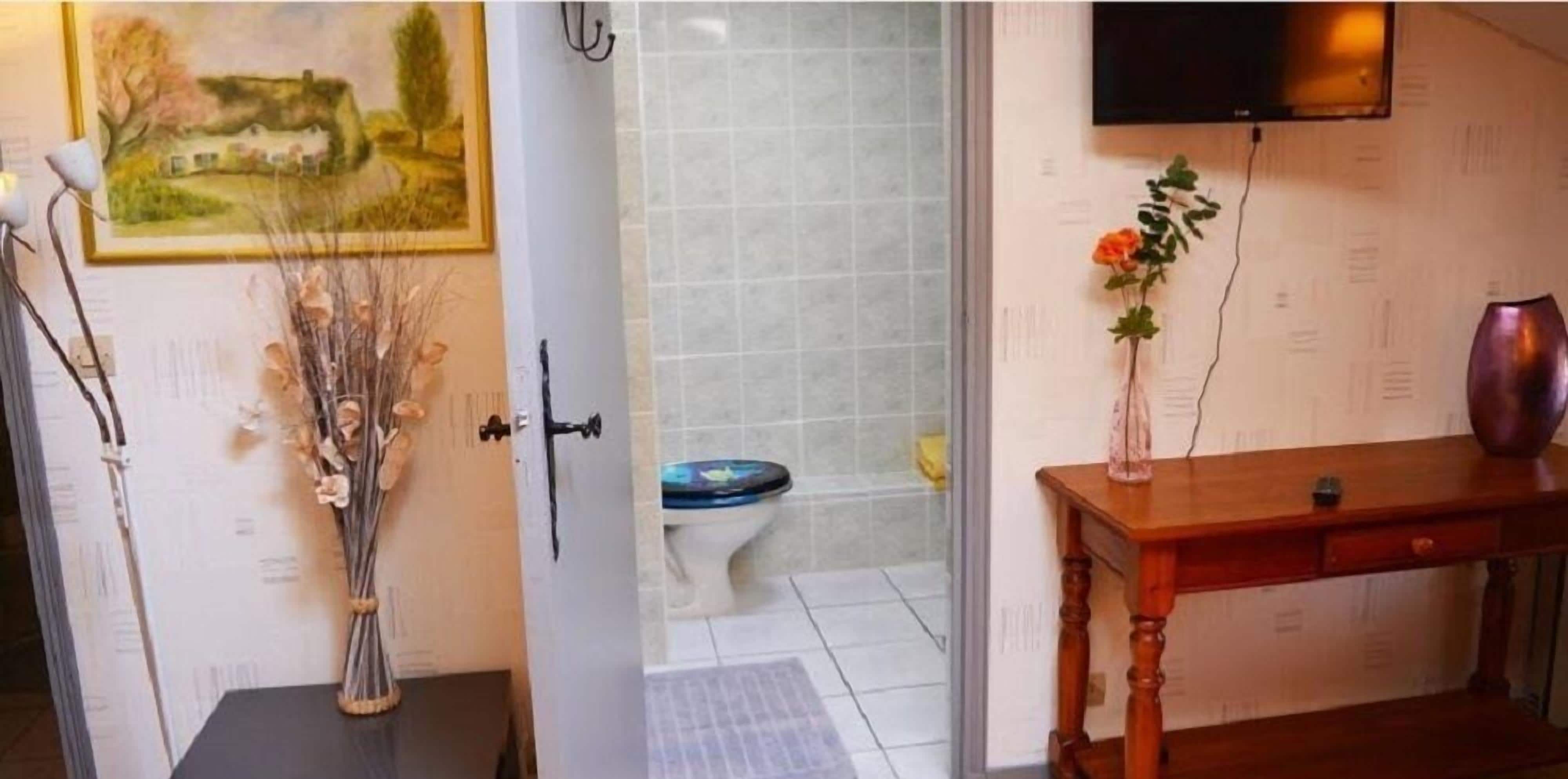 Un baño con inodoro, ducha, una mesa de madera con un florero y un cuadro en la pared.