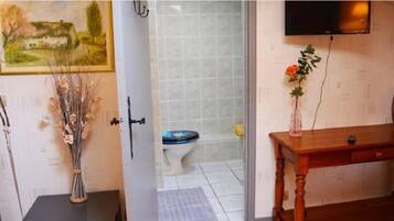 Un baño con inodoro, ducha, una mesa de madera con un florero y un cuadro en la pared.