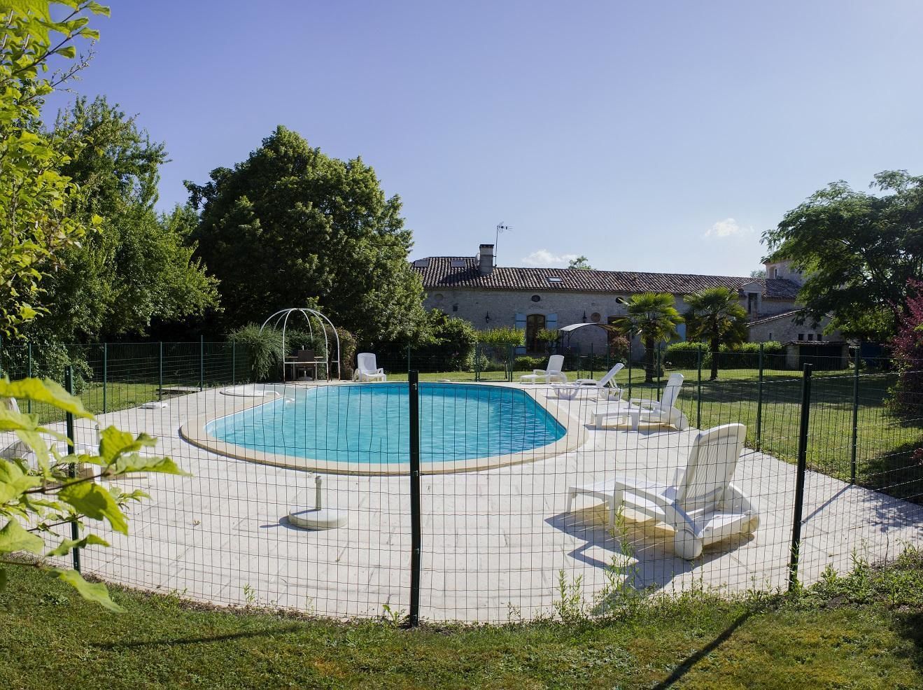 Una piscina con una terraza alrededor, sillas de descanso y una valla.