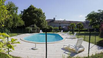Una piscina con una terraza alrededor, sillas de descanso y una valla.