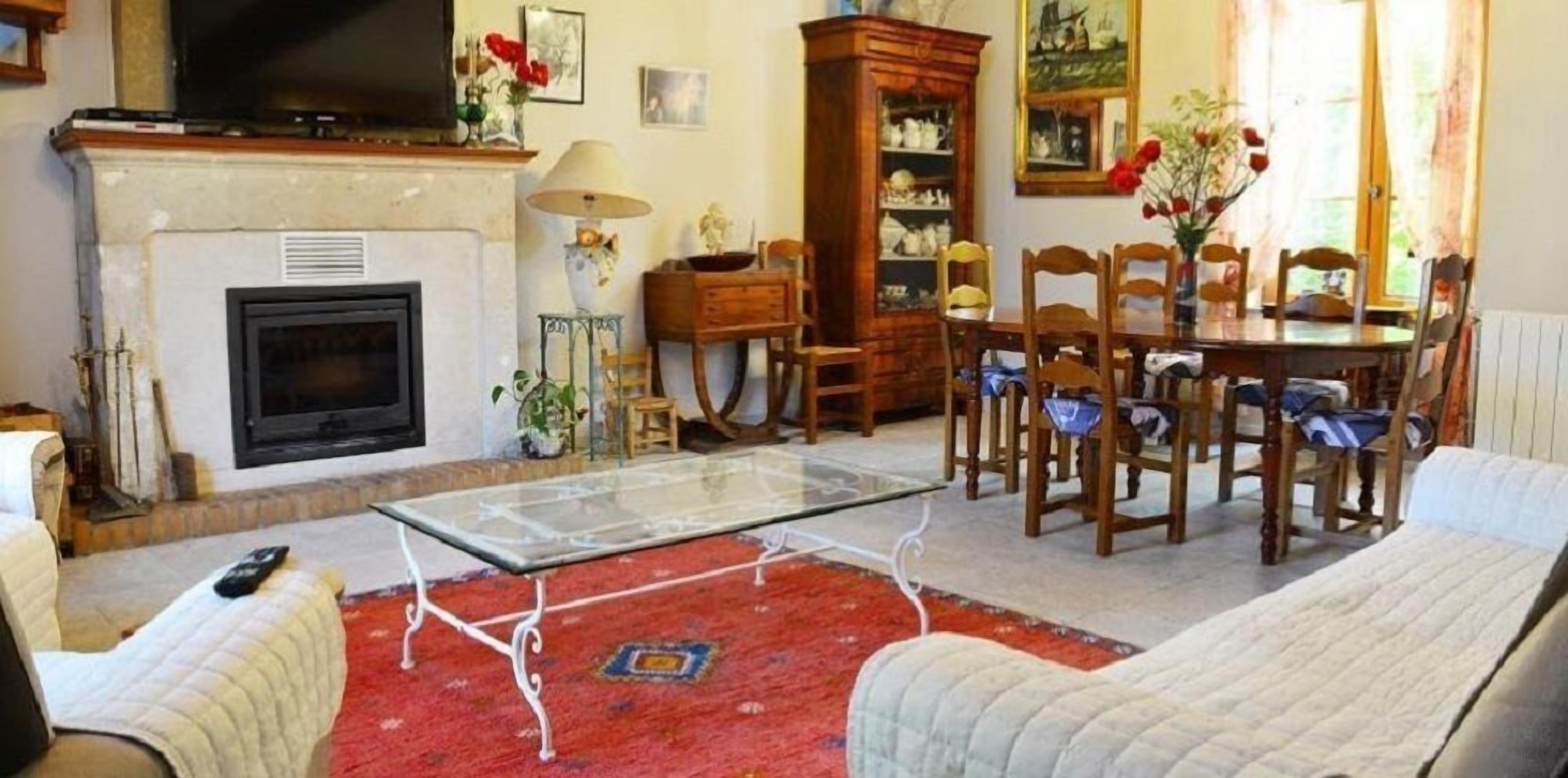 Een woonkamer met een open haard, een glazen salontafel, een eettafel met stoelen en een bank.