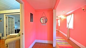 Un couloir aux murs roses, orné d’un miroir rond et d’un tapis rayé aux couleurs vives.