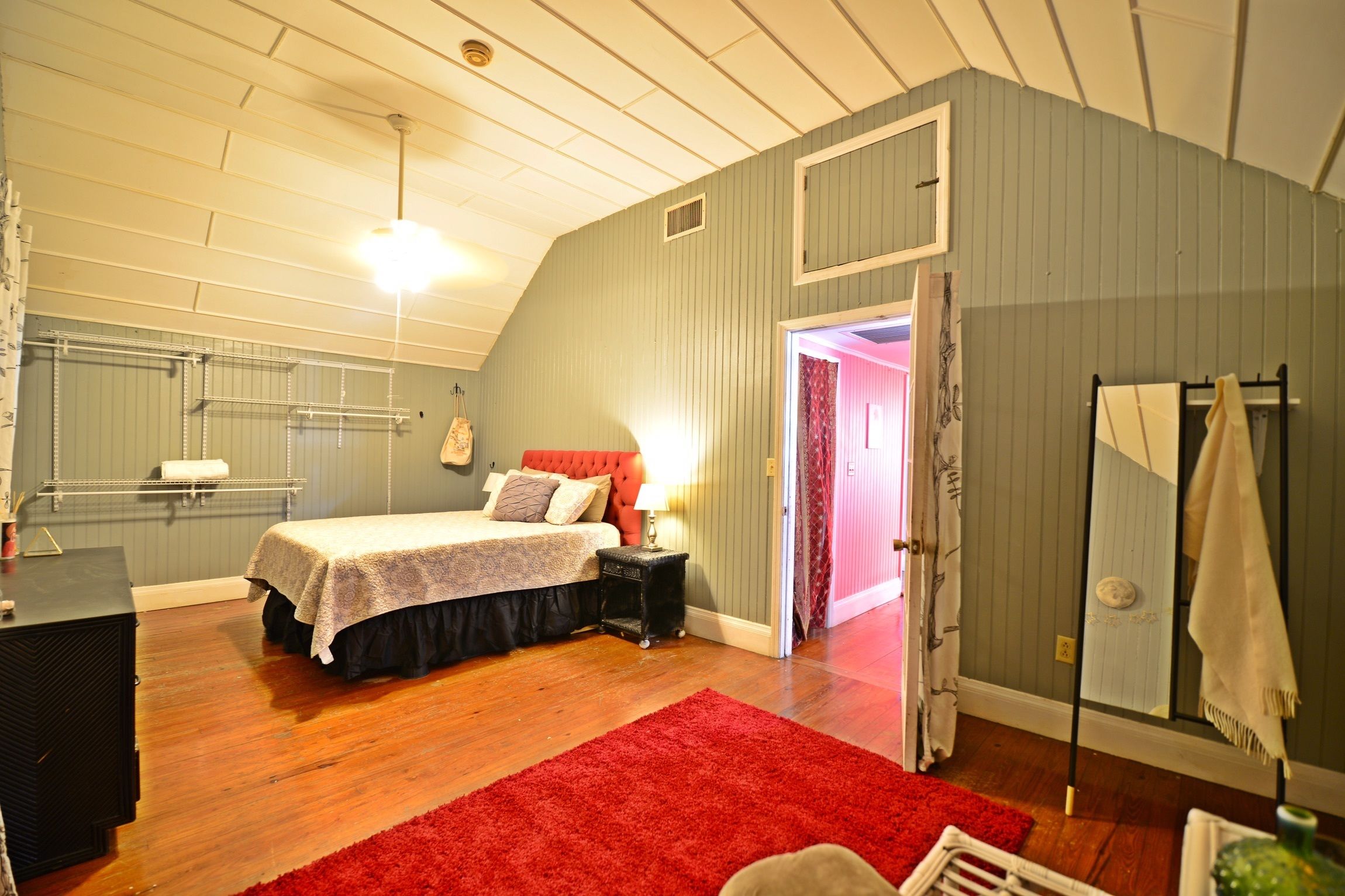 Een slaapkamer met een bed, een rood tapijt, een nachtkastje, een spiegel en een kledingkast.