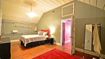 Een slaapkamer met een bed, een rood tapijt, een nachtkastje, een spiegel en een kledingkast.