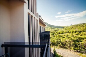 A modern building with a balcony overlooking a lush green landscape and distant hills.