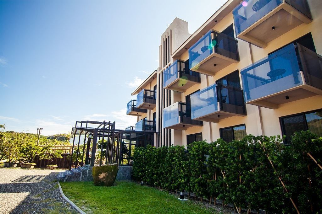 A modern multi-story building with balconies, a covered outdoor area, and a well-maintained garden.