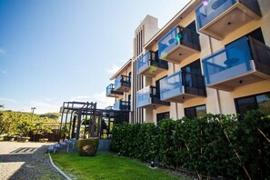 A modern multi-story building with balconies, a covered outdoor area, and a well-maintained garden.