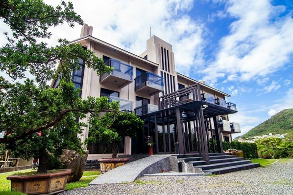 A modern hotel with a multi-story structure, outdoor seating area, and a well-maintained garden.