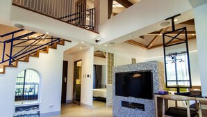 A spacious living area with a staircase, a TV mounted on a tiled wall, and a dining area with a wooden table and chairs. - Siangge Chuanfan Rock Resort (Hengchun)