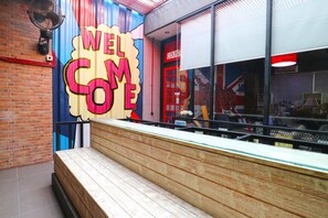 A reception area with a 'WELCOME' sign, a wooden bench, and a glass partition. - Kamariska Hostel (Sidoarjo)