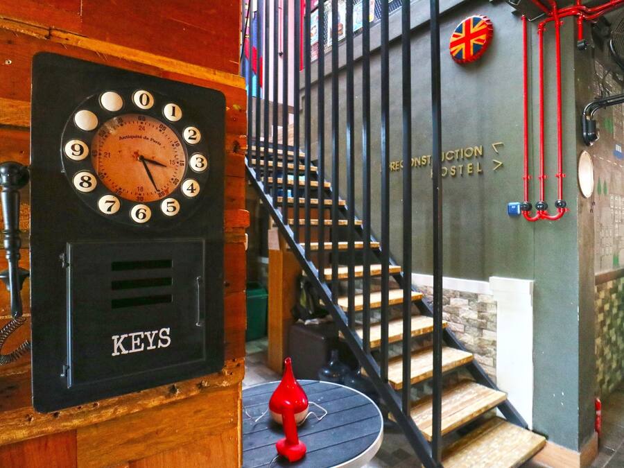 A wall-mounted clock with a keyhole below it, a staircase with a Union Jack flag, and a sign indicating a hostel.