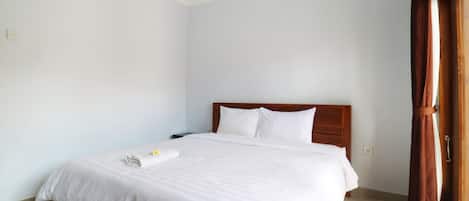 A neatly made bed with white linens and pillows, a wooden headboard, and a wooden door with a curtain.