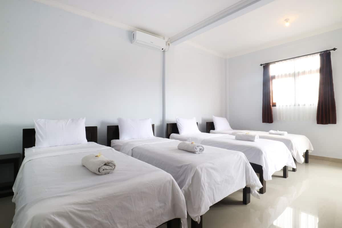A hotel room with four single beds, white bedding, a ceiling air conditioner, and a window with curtains.