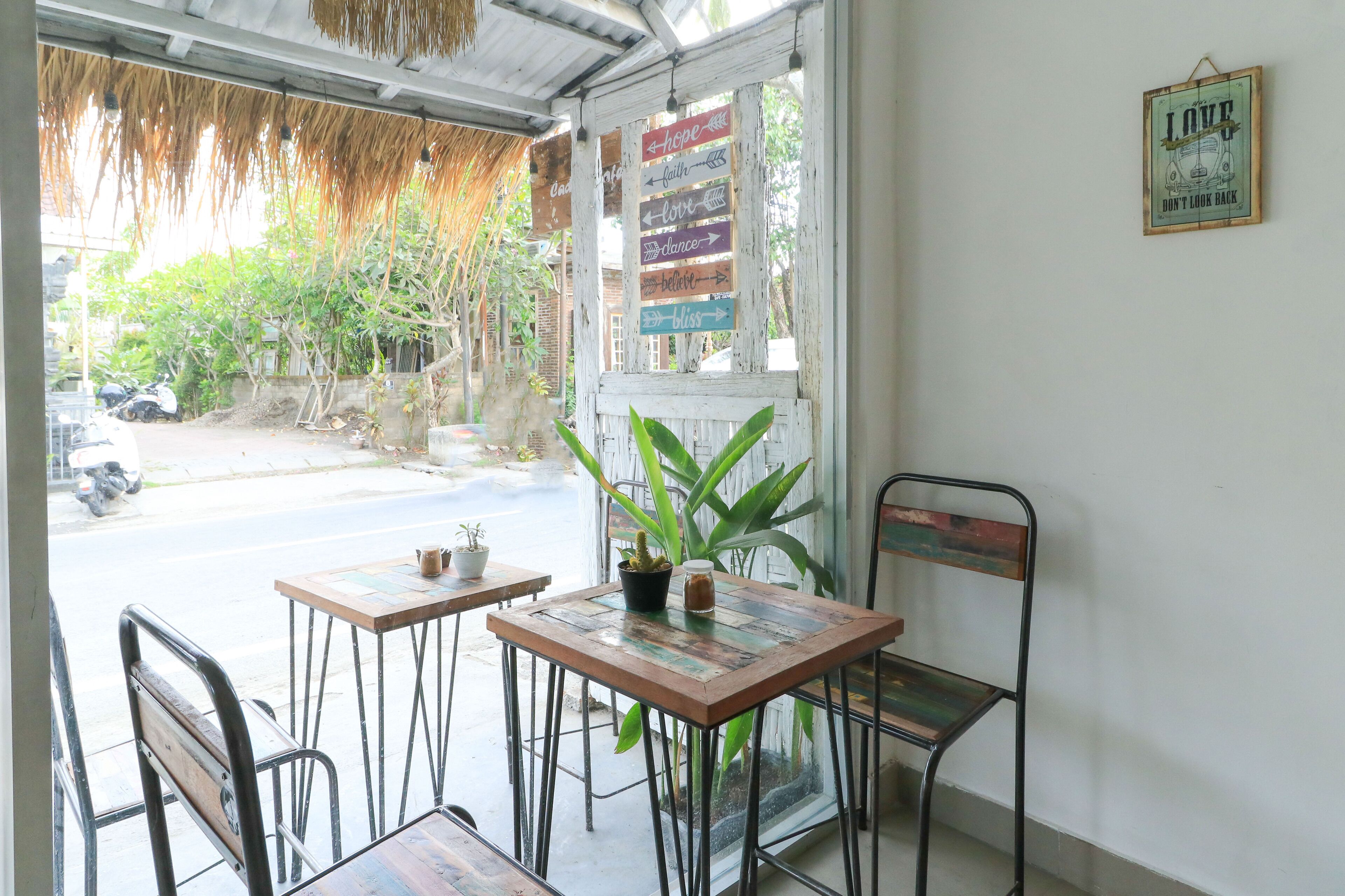 A cafe with two tables and chairs, a potted plant, and a sign with motivational phrases.