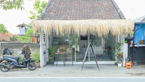 A building with a thatched roof entrance, a motorcycle parked outside, and a small table and chair set up in front. - The Wina Echo Beach Guesthouse (Canggu)