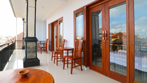 A balcony with wooden furniture and a view of buildings. - The Wina Echo Beach Guesthouse (Canggu)
