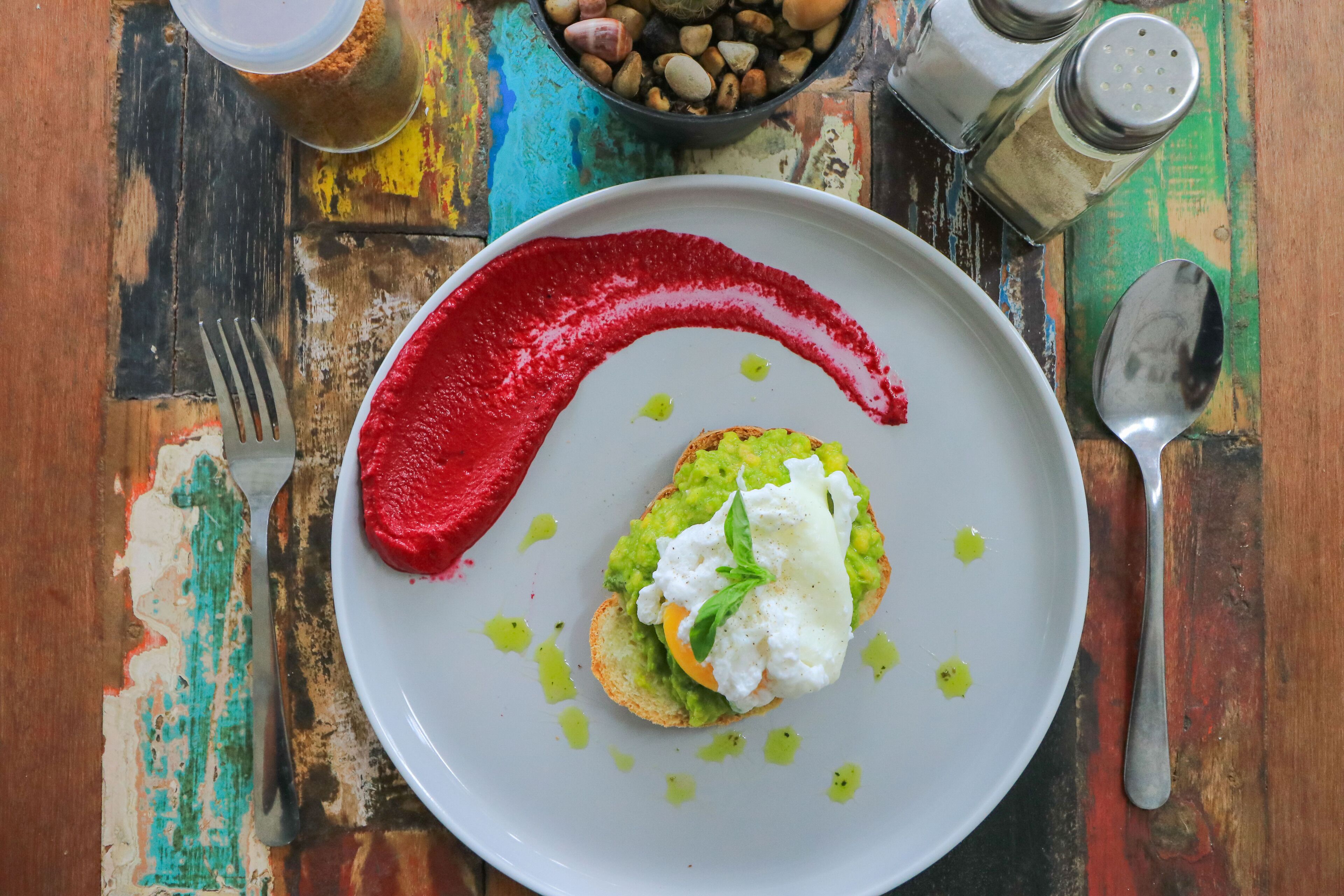 Un plato con tostada de aguacate cubierta con un huevo pochado y salsa roja.