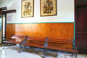A wooden bench with metal armrests in a hallway with a wooden panel wall and a green trim. - Hotel Shabine (Surabaya)