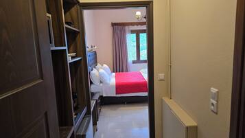 A hotel room with a bed, a window with curtains, a radiator, and a door leading to a hallway.