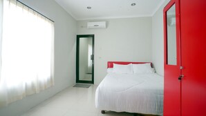 A bedroom with a bed, a red door, and a window with curtains.