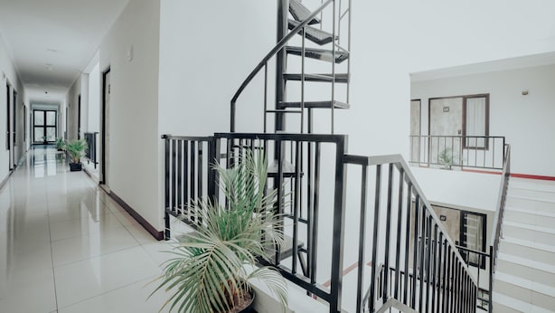 A modern hotel interior with a central staircase, potted plants, and a clean, bright hallway.
