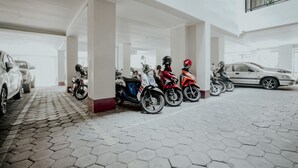 A parking area with multiple motorcycles and cars, featuring a hexagonal tile floor and white pillars.