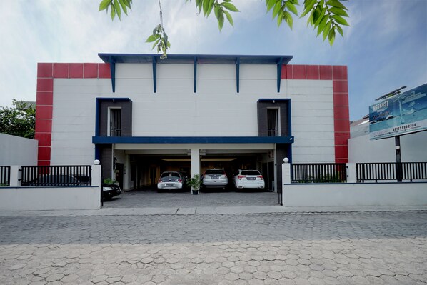 Un edificio con fachada blanca, detalles en rojo y un estacionamiento cubierto con tres coches.
