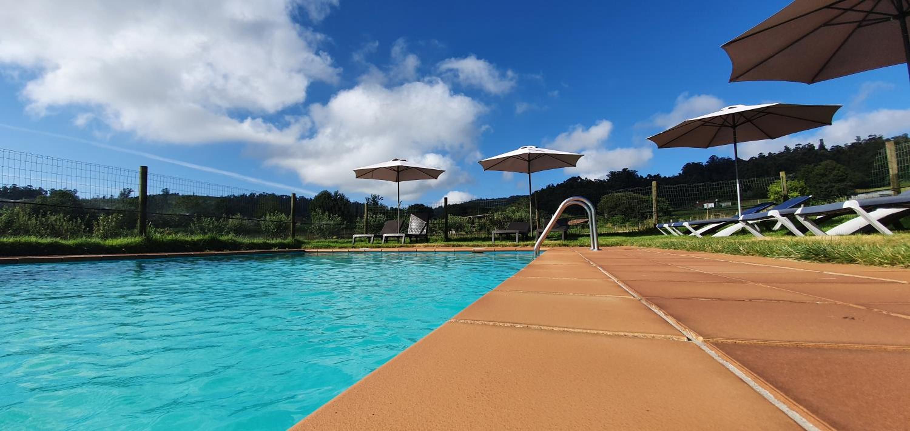 A swimming pool with a clear blue water surface, a sunshade, and a poolside area.
