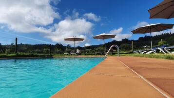 A swimming pool with a clear blue water surface, a sunshade, and a poolside area.
