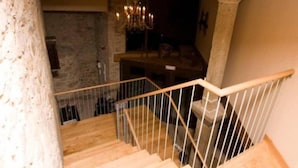 A wooden staircase with a metal railing, leading to a stone wall and a chandelier.