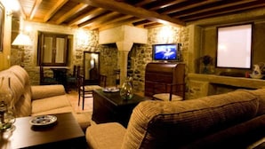 A cozy living room with stone walls, wooden beams, a television, and comfortable seating.