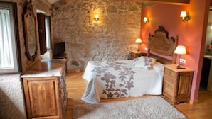 A bedroom with a stone wall, wooden bed frame, two bedside tables with lamps, and a large mirror on the left.