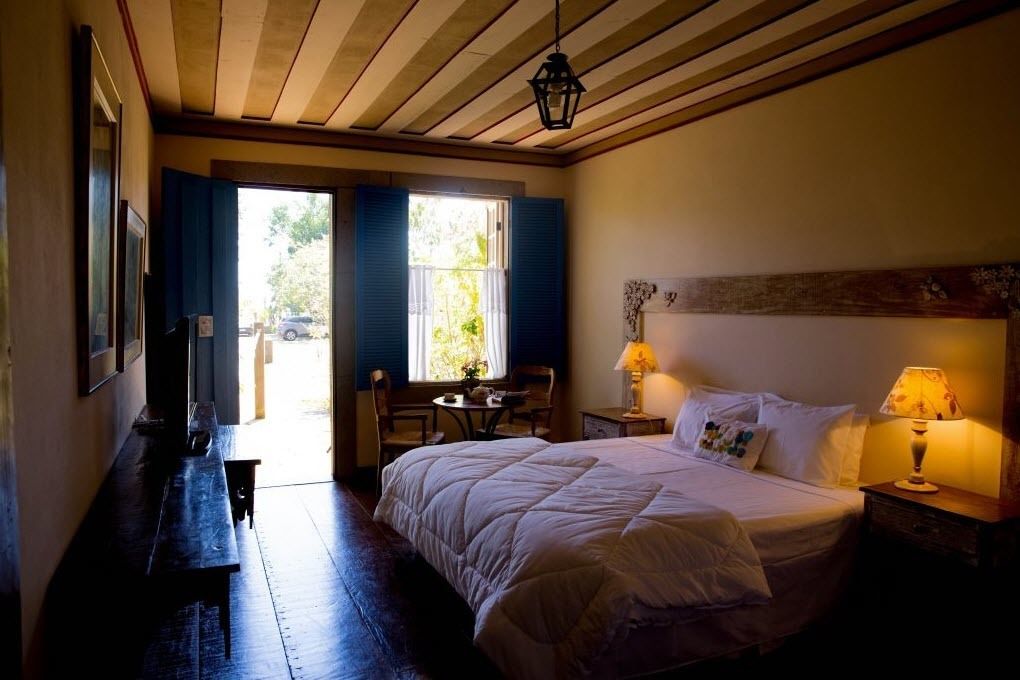 A bedroom with a bed, bedside lamps, a window with curtains, a desk, and a chair.
