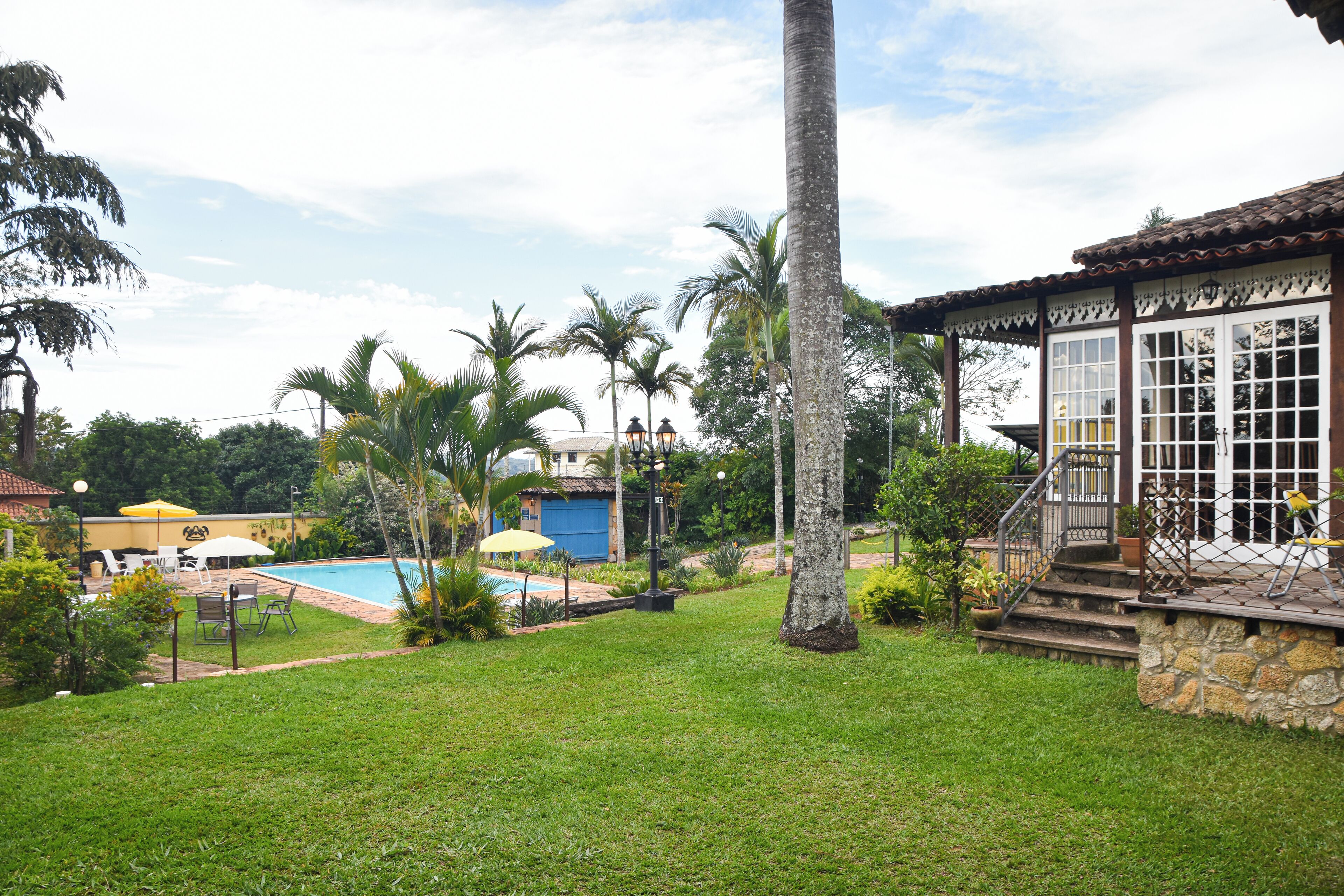 Zona de piscina con césped, palmeras y un edificio con tejado de baldosas.