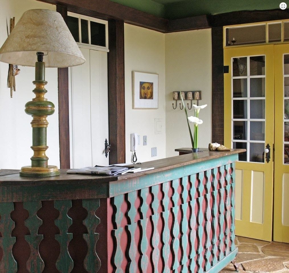 A reception desk with a lamp, framed artwork, and a vase with flowers.