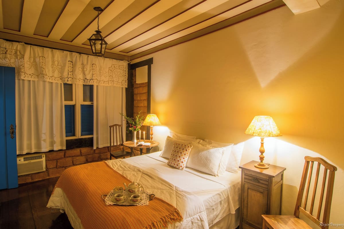 Ein ordentlich eingerichtetes Schlafzimmer mit Bett, Nachttischen, einer Lampe und einem Fenster mit Vorhängen.