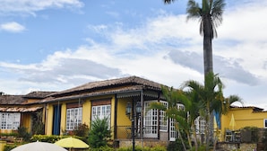 Un edificio amarillo con techo de tejas, una palmera y mesas exteriores con sombrillas.